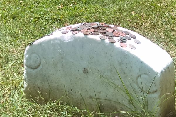 People place pennies on the blank headstone.